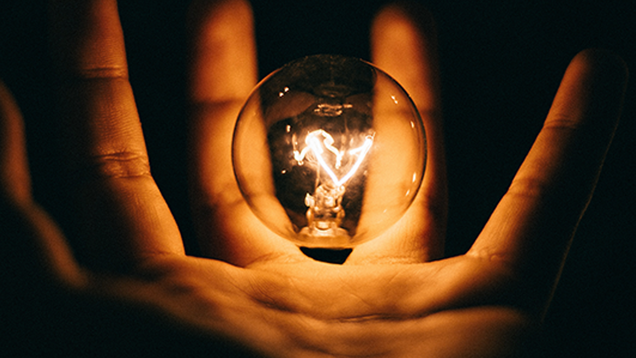 Hand holding a lightbulb with dark dramatic background